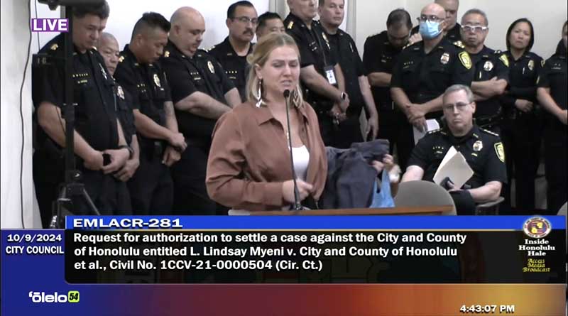 Lindsay Myeni, the widow of Lindani Myeni, who was killed by police in 2021, held up the bloodied shirt he was wearing the night he was shot as she testified before the City Council on Wednesday. (Screenshot/Olelo TV/2024)